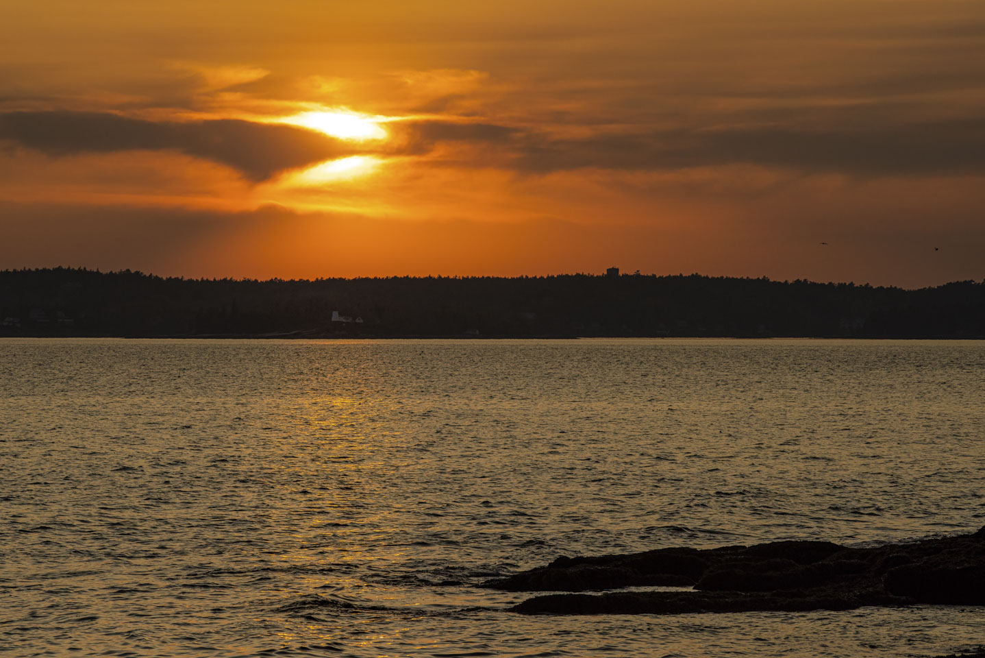 The sun is bisected by clouds, and Brant Rock Lighthouse is visible