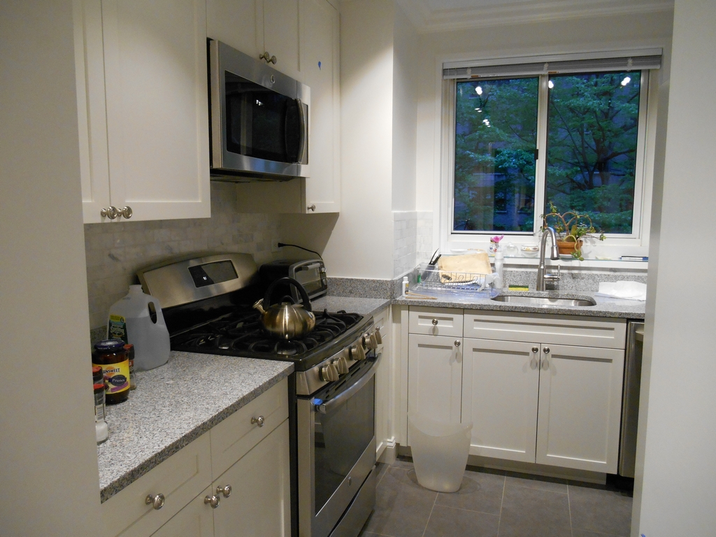 Newly renovated kitchen with white cabinets, gray counters, subway-tile backsplash, and a window above the sink