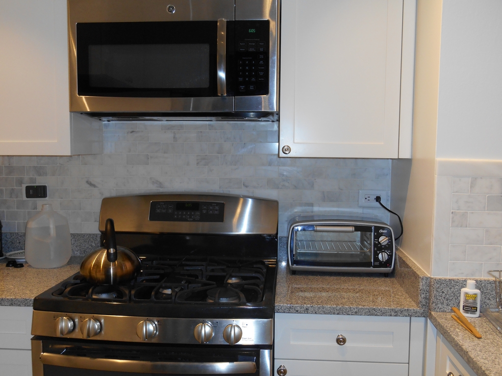 Closer view of the stove, microwave, toaster oven, and pale subway-tile backsplash in the renovated kitchen