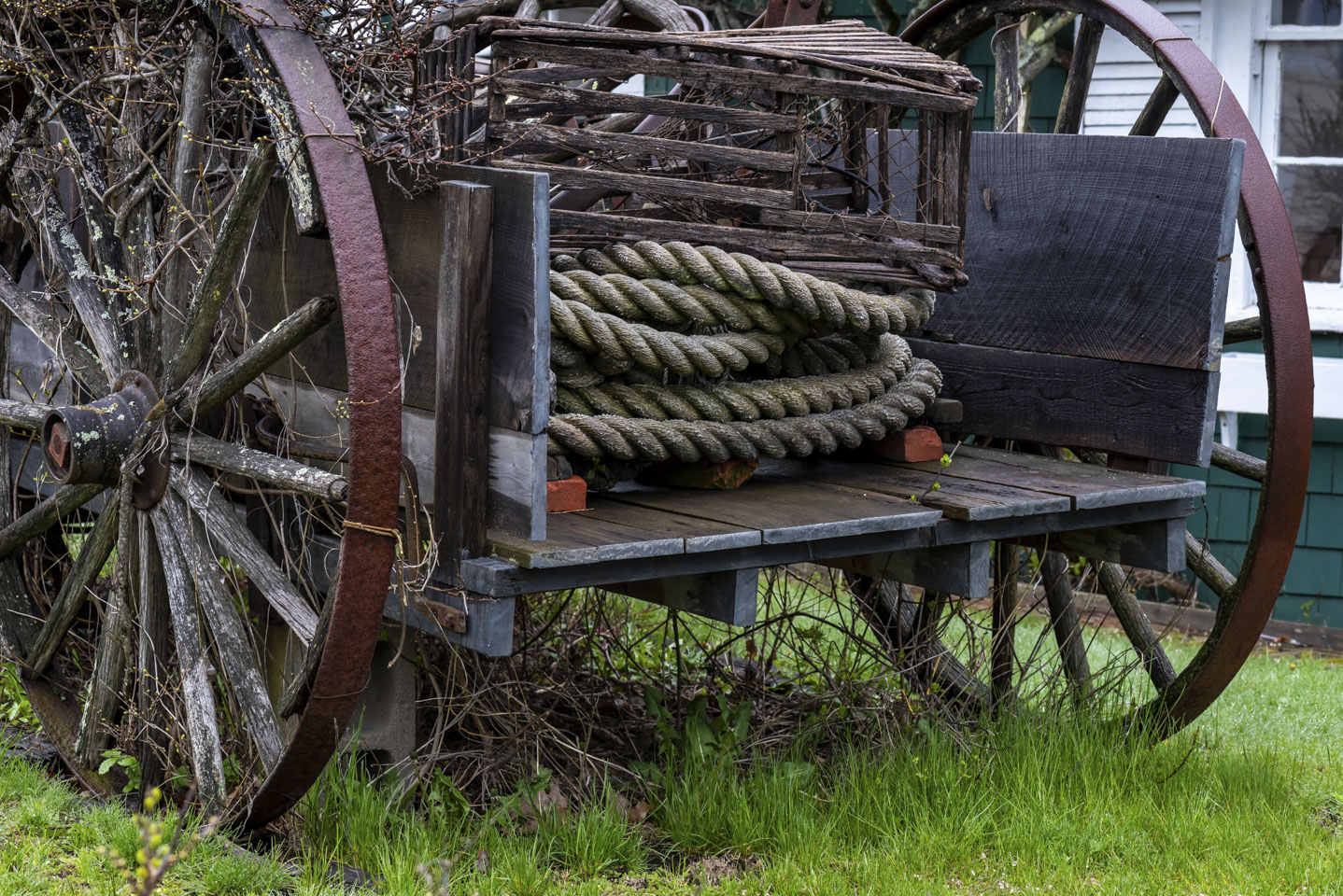 An old wagon with large wheels, with rope and a crate in the back