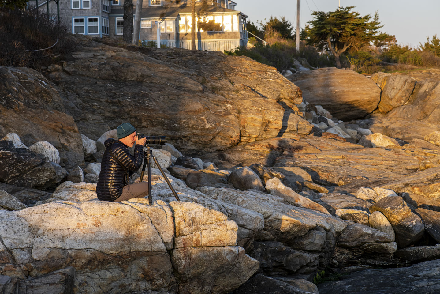 Paul sitting on rocks at Ocean Point as sunset, taking a photograph