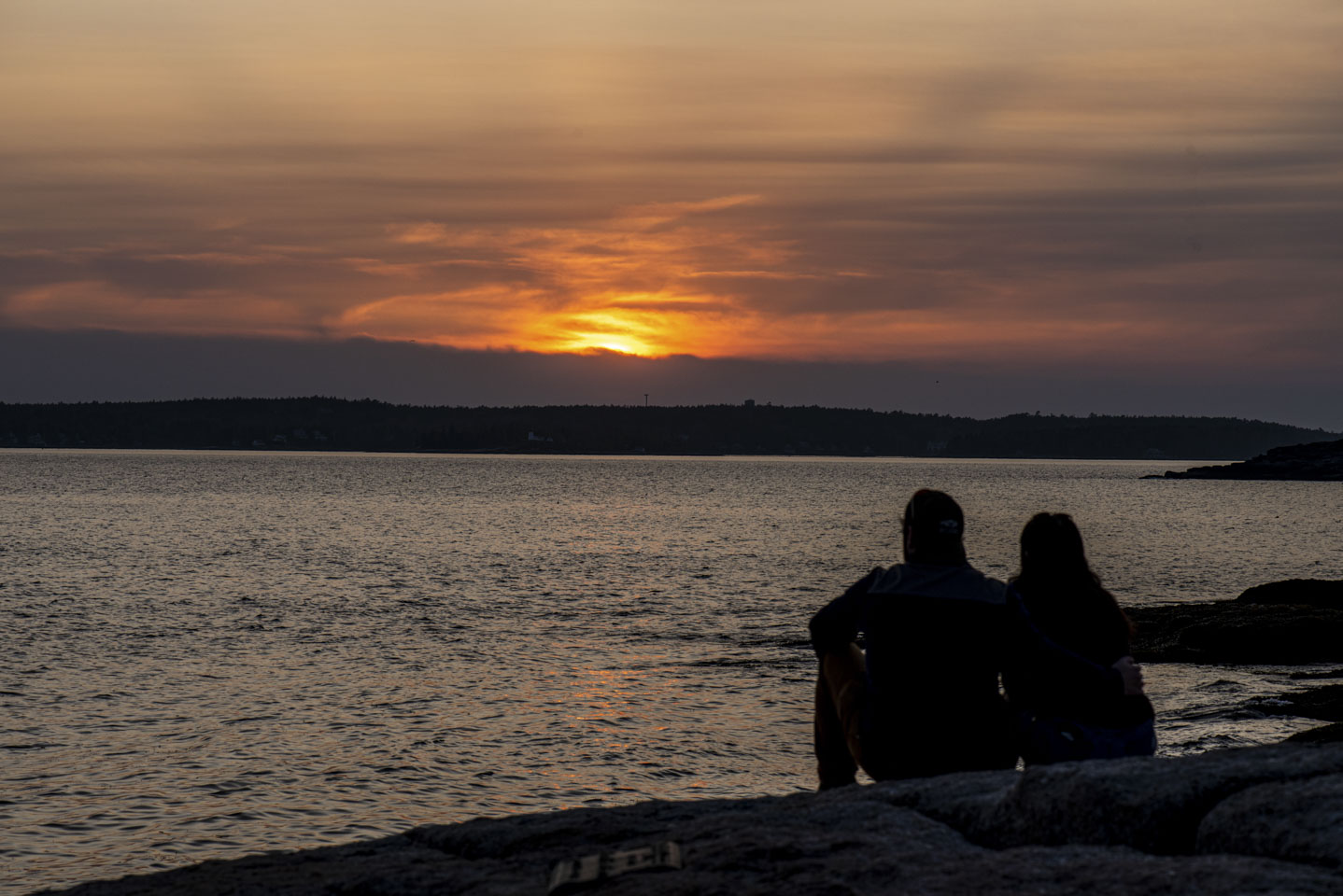 Couple sitting on the rocks watching a sunset