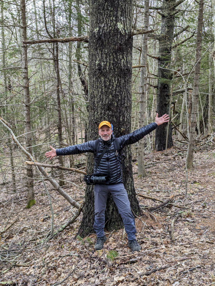 Paul standing in front of a tree, with his arms outstretched much wider than the tree.