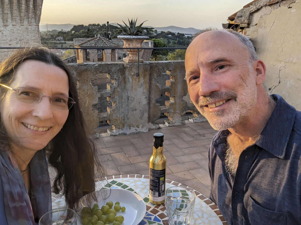 A selfie of Anne and Paul with a bottle of olive oil and some grapes