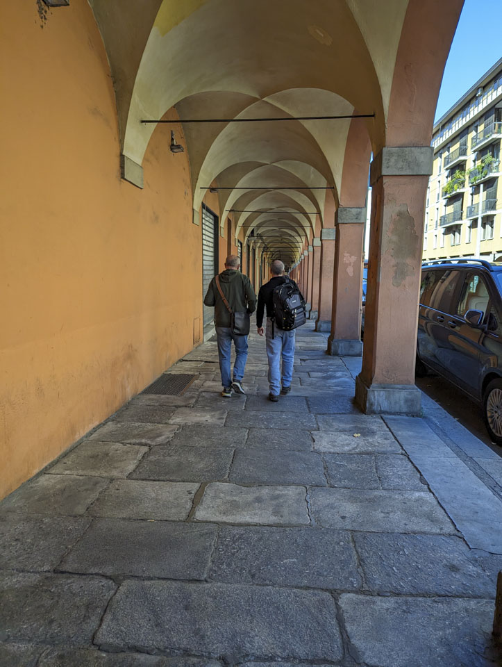 Two men seen from the back walking on a covered walkway in Bologna, Italy.