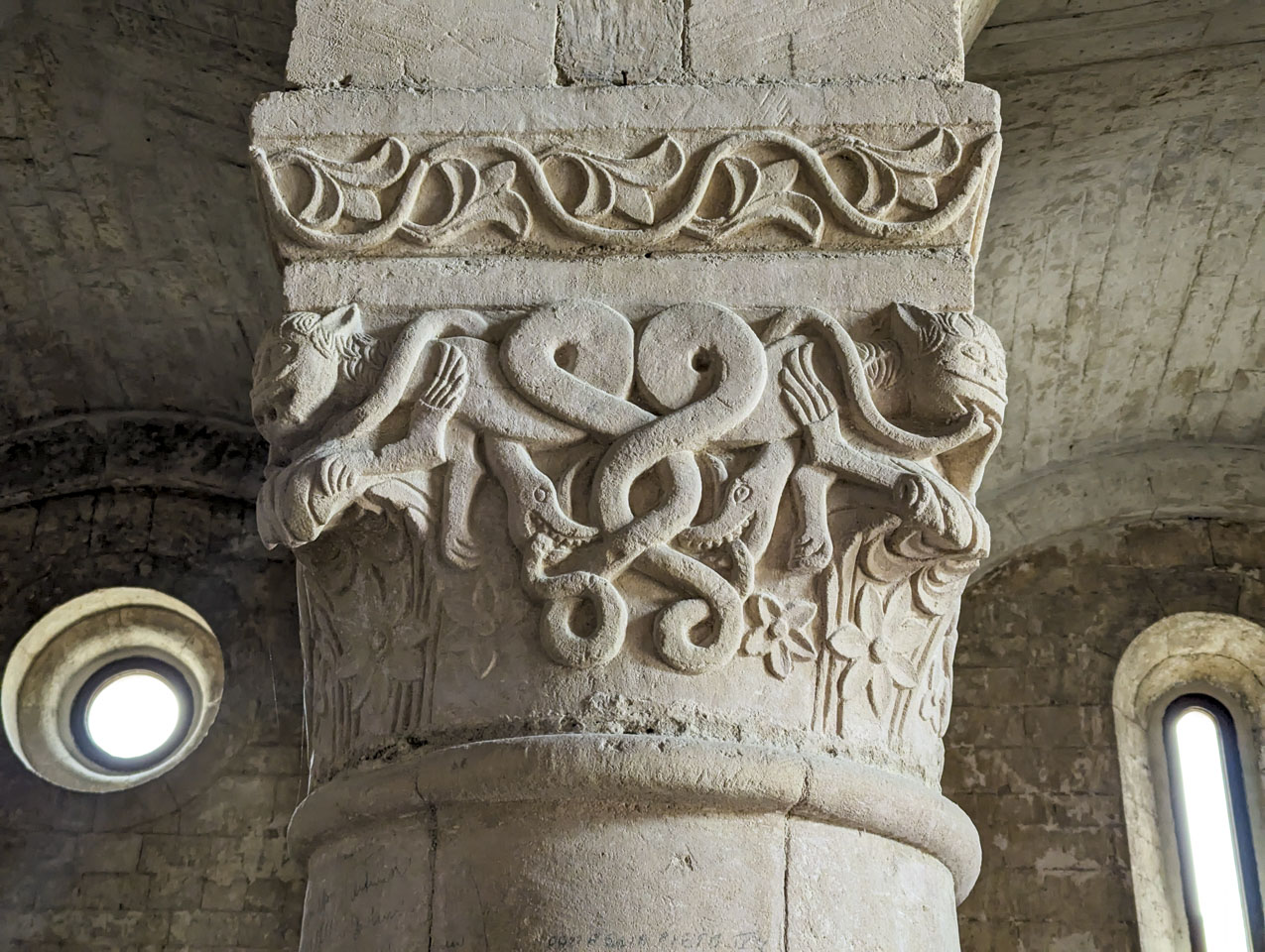 A close-up picture of the top of one of the columns. It has a complex design of snakes, flowers, and faces.