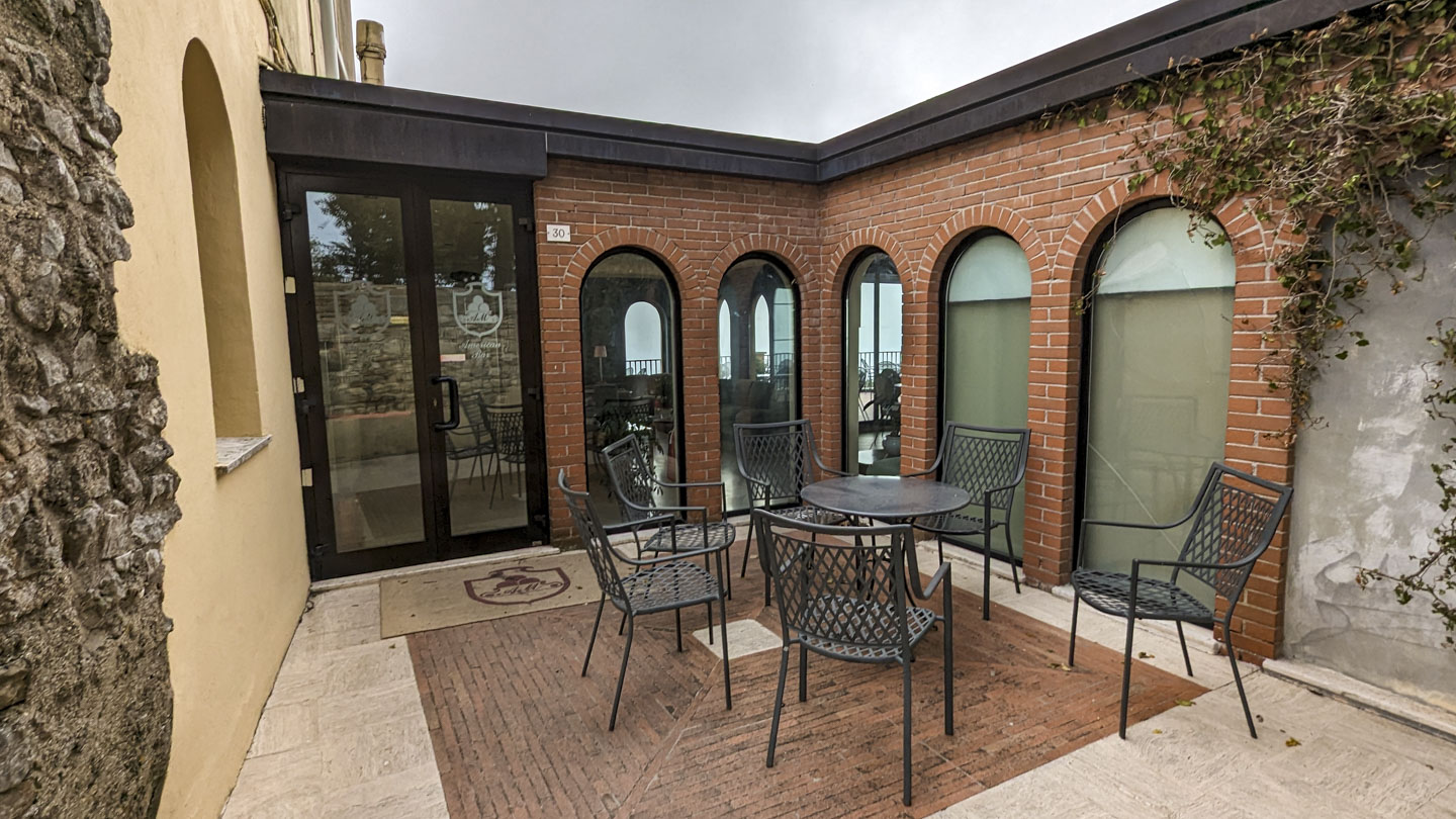 An alcove off the main courtyard with a round metal table and 6 metal chairs around it.  The walls are modern brick with large windows and a glass door.