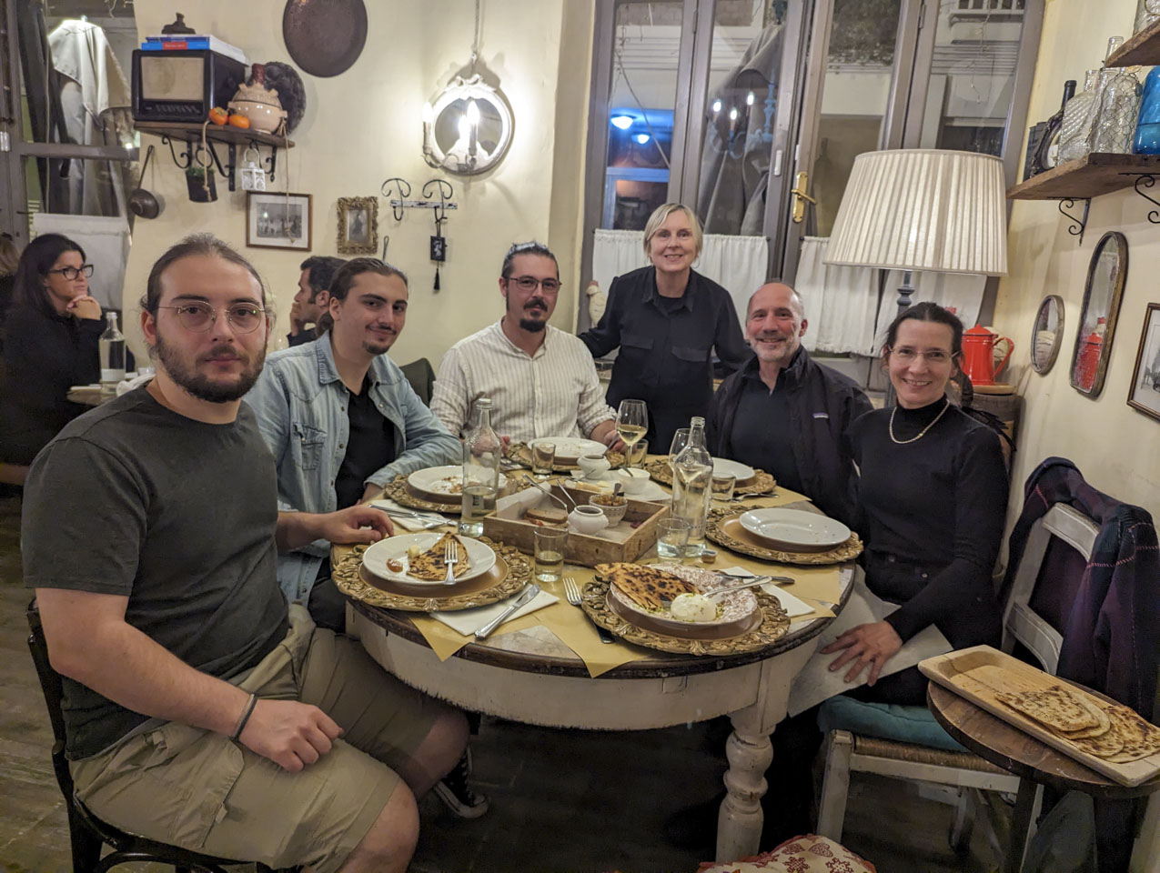 6 people at an oval table, with some appetizers on the table that consist of cheese and flat bread.