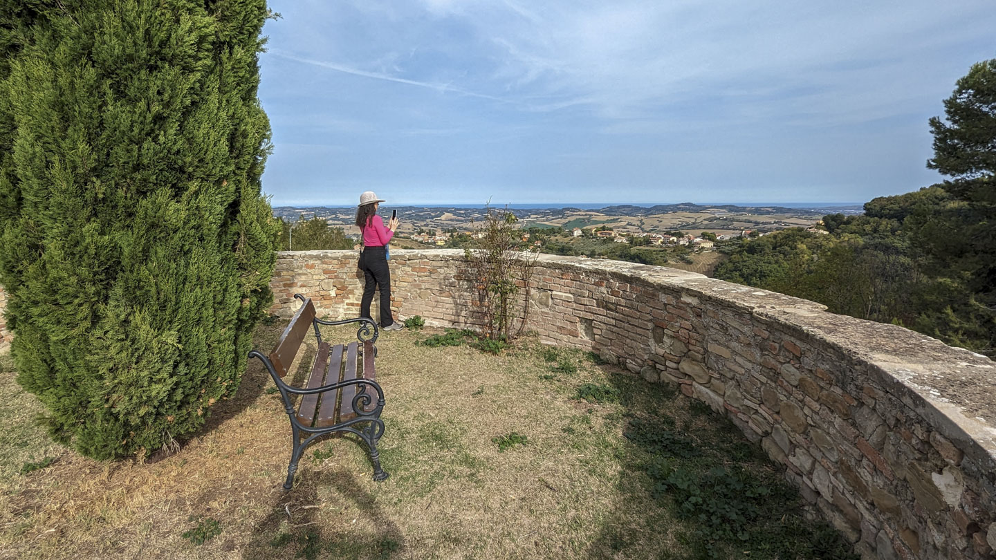 Anne standing near a bench and looking out over a wall to the Marche countryside.