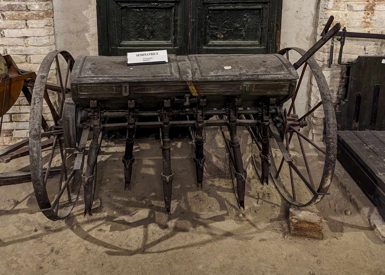 A device with a large wheel on each side of a shallow covered chest. Protruding down from the chest are 6 tubes to put seeds into a furrow.