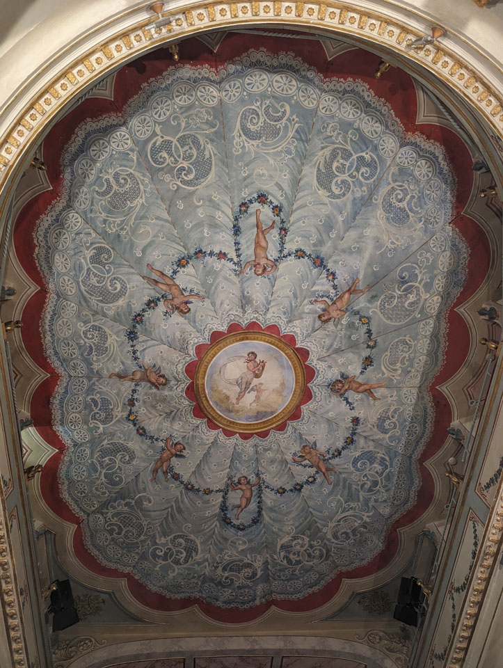 Ceiling painting that looks like lace with cherubs and Apollo holding a lyre in the center.