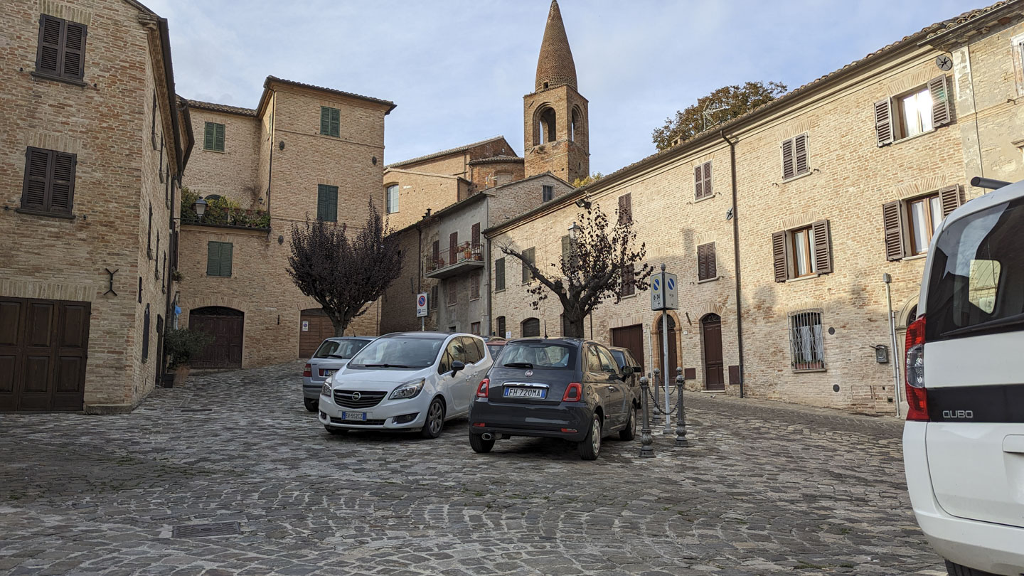 Piazza in Mondavio with some parked cars and a tower in the background