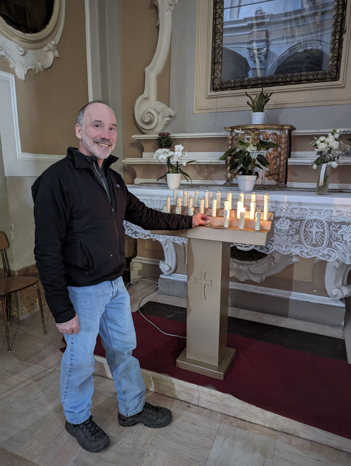 Paul putting a donation into the box at a church, with only 1 electric candle lit