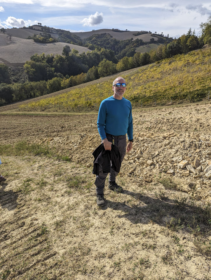 Paul standing on a sloped field next to a tilled area that reveals chunky soil.
