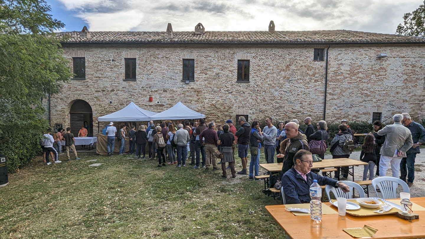A large stone wall of the old convent building with a line of people going towards a couple of tables. In front are some tables for participants to eat at.