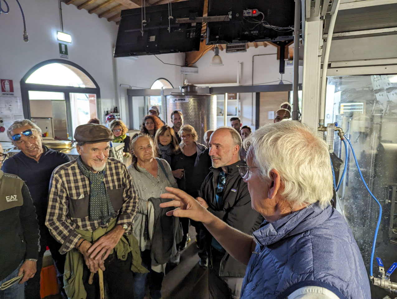 A group of people listening to a man talking inside the olive processing area of the cantina.