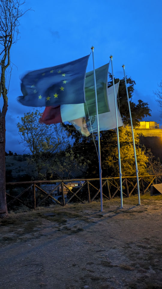 Three flags on individual flagpoles are straight out due to the wind.