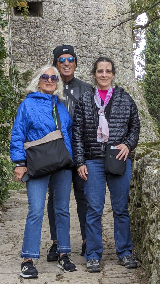 Alizia wearing a blue jacket, Roberto wearing a black jacket and a hat, Anne wearing a black jacket. A stone wall is behind them.