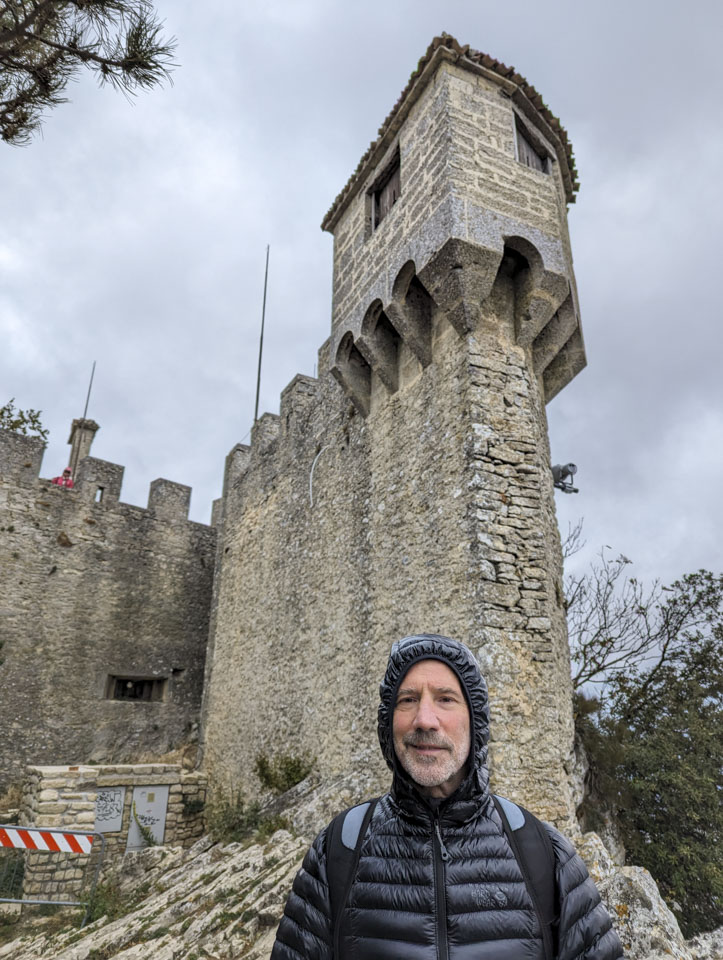 Paul wearing a warm jacket with a tower and wall looming behind him.