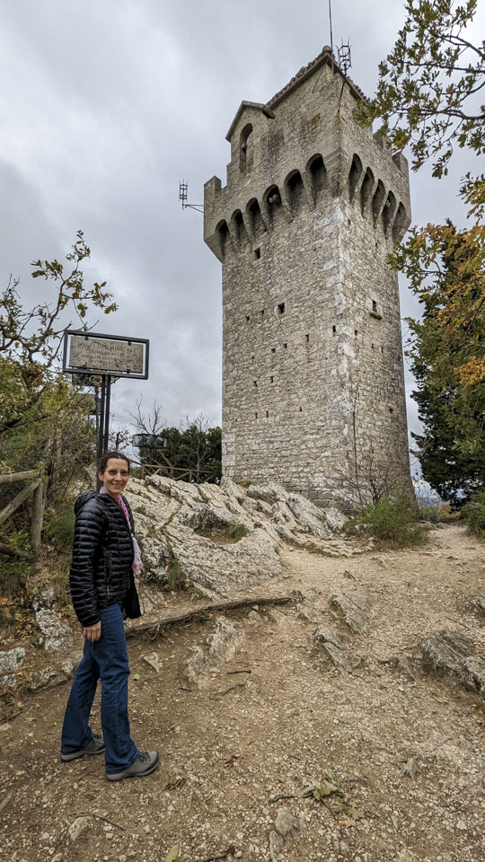 Anne is looking back towards the camera with a tall tower a bit further away.