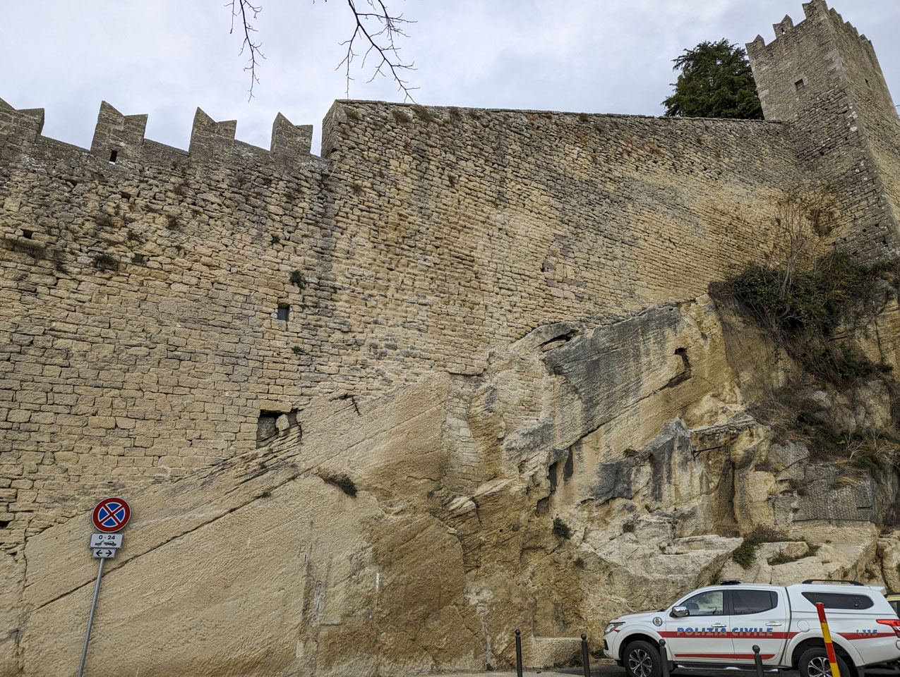 A civil police vehicle is seen on the lower right, then an angled rock wall with a tower at the top right.