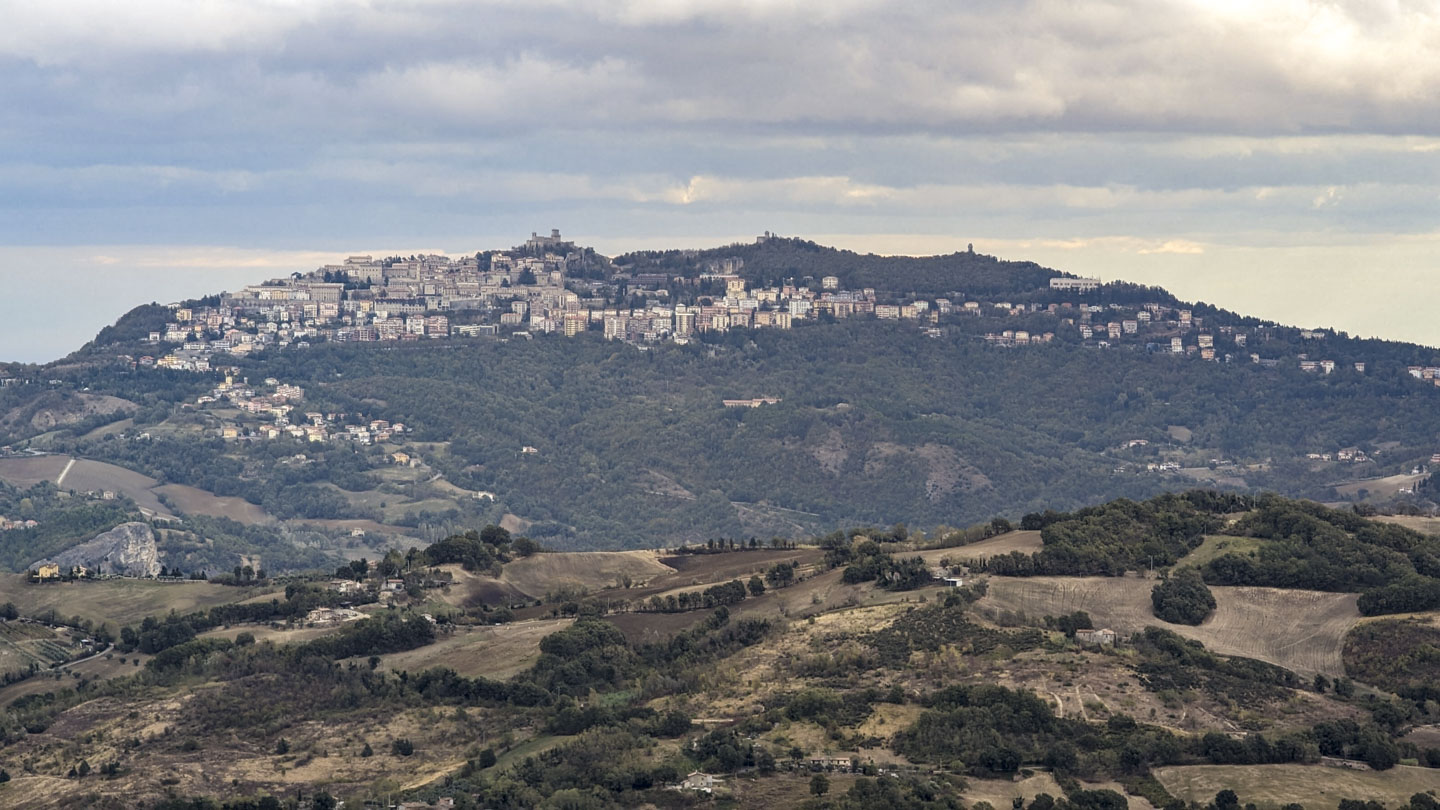 A lower ridge is in front, and a high ridge in the distance.  Near the top of the ridge is a village, mostly on the left, with many layers of houses.