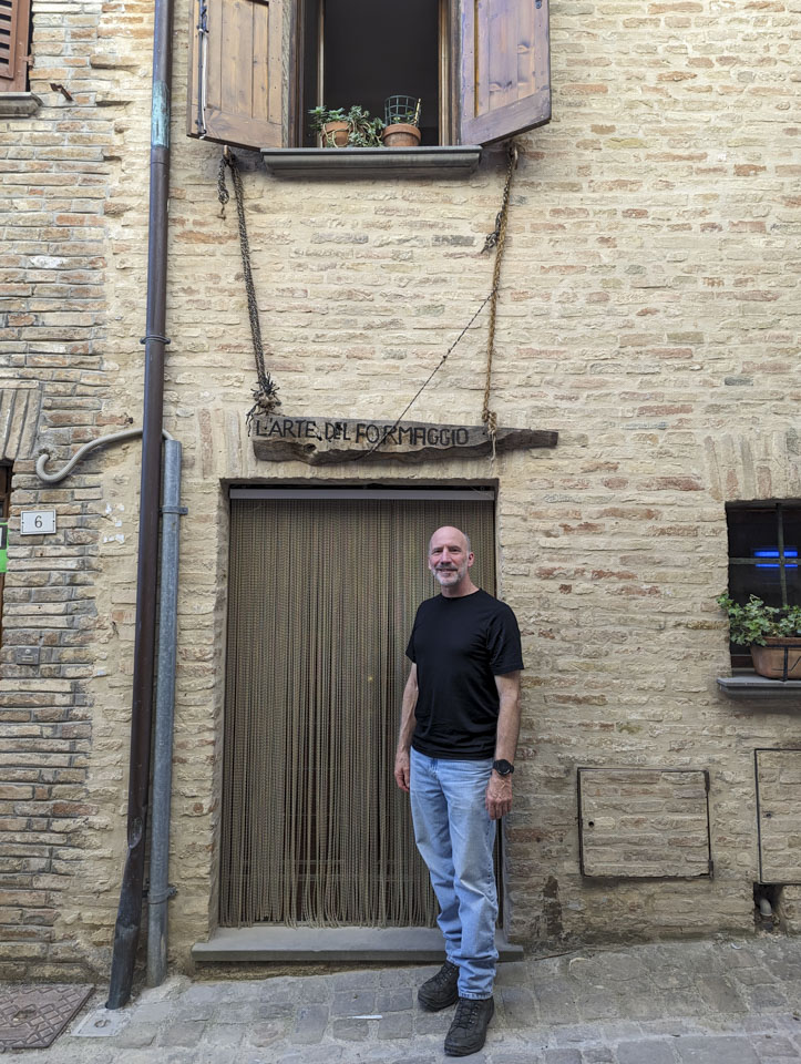 Paul in front of a door with a sign above it that translates as The Air of Cheese