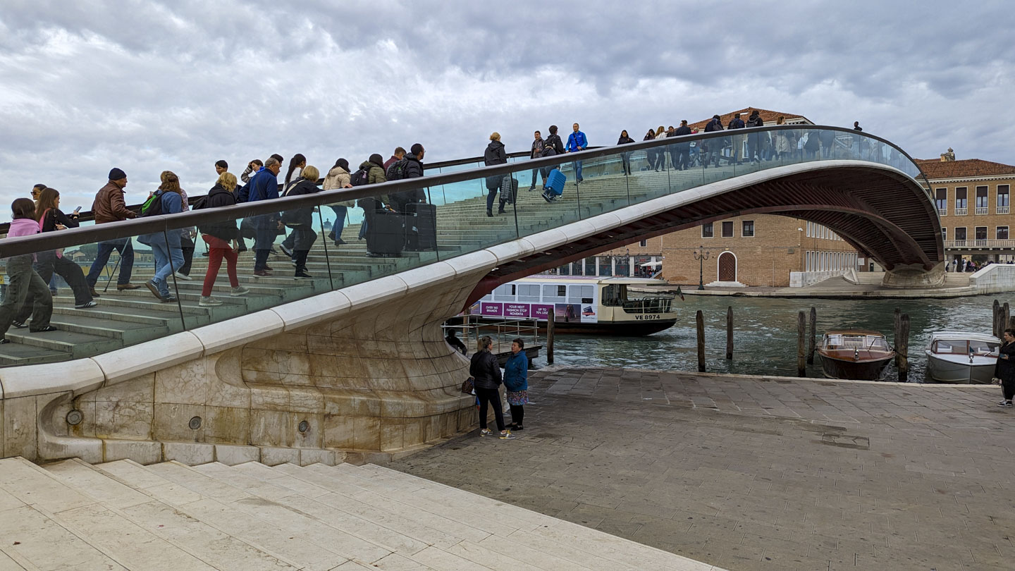 A graceful looking pedestrian bridge with glass railings and steps, with a boat going underneath the bridge
