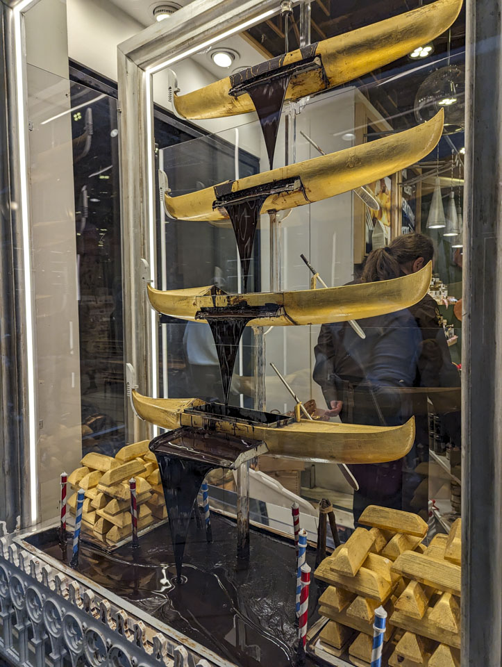 Four yellow model gondolas stacked so that chocolate can flow from each to the one below, and finally into a pool of chocolate.