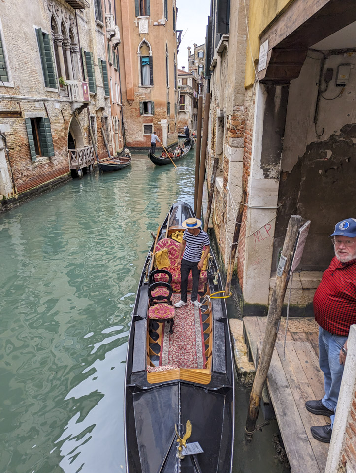 Gondola in the water with a gondolier, and a man in a plaid red shirt standing on a boarding platform 