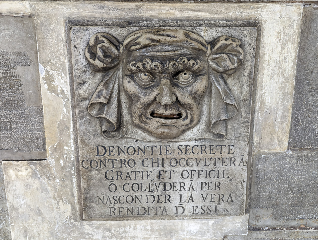A close up of the carved face, with curling eyebrows and a cloth head covering that drapes down behind the head.
