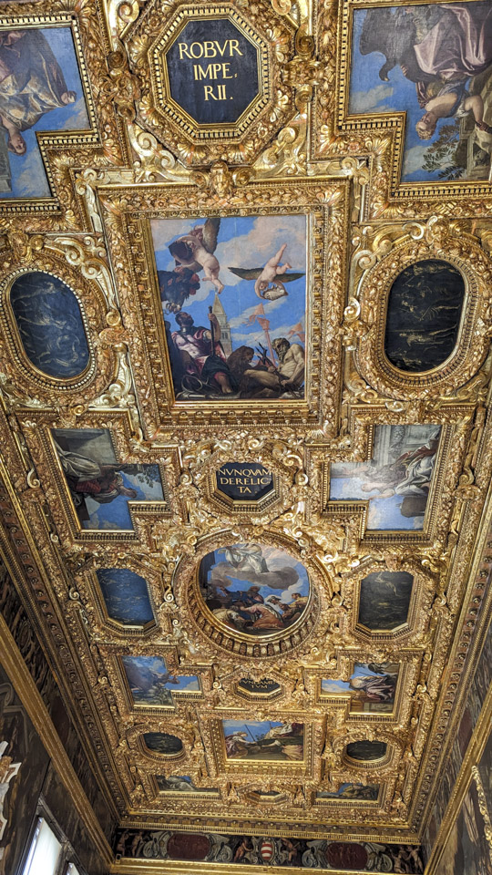 A picture of the ceiling, with gold colored framing and many paintings in recessed panels.