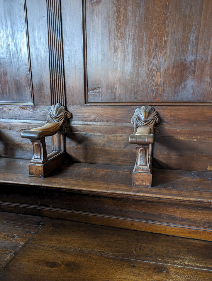One of the built-in wooden seats, with lightly padded armrests and a plain wooden sitting area.