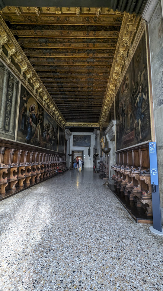A long wide hall with seats on both sides and paintings on the walls.