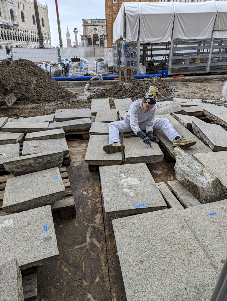 A woman in a white workers outfit cleaning a stone slab, with many other stones around her.