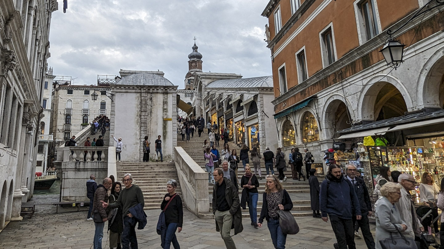 A view from the northwest side of the Rialto bridge. There are many steps that split to go around a wall. You can see on the other side of the center walkway shop fronts that are within the structure.