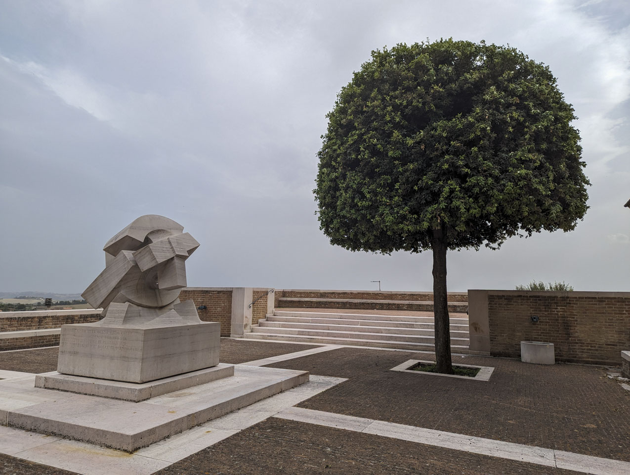 sculpture of curves and lines on the left and a neat and trimmed tree on the right of the photograph