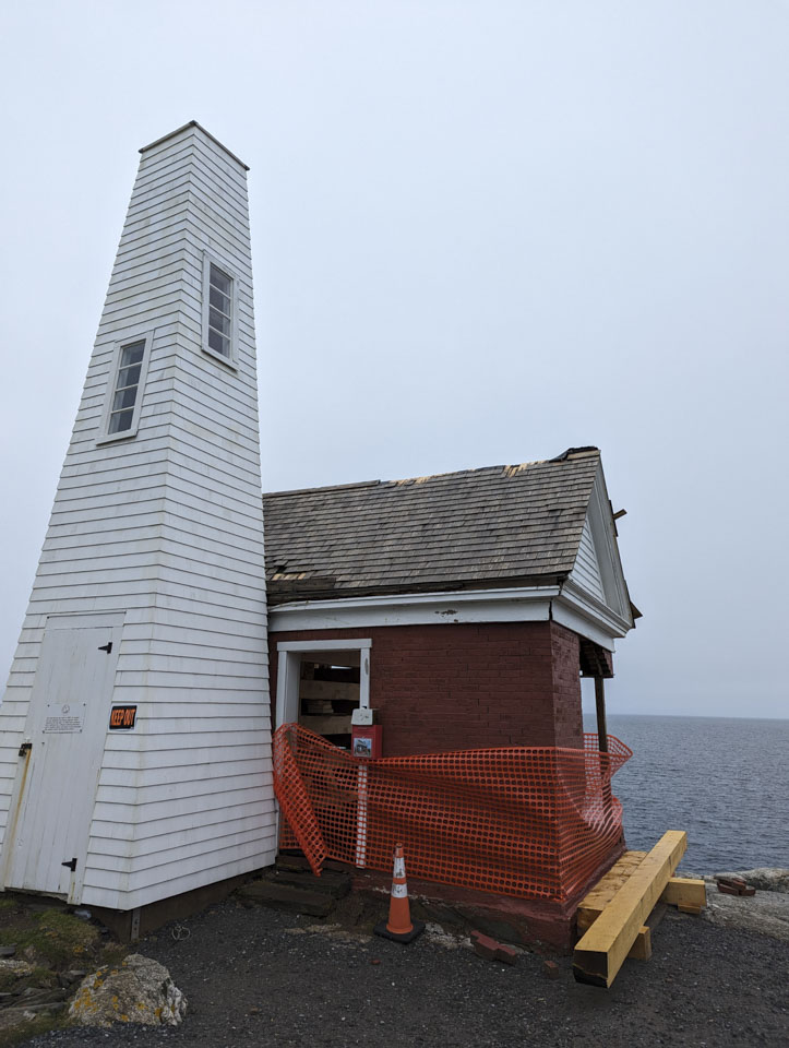 The bell house has a little white tower and a brick red section, but many of the bricks are missing and the roof is damaged. 