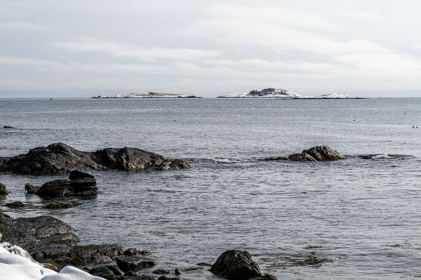 Two snow-covered islands are in the distance, while some rocks are in the water closer in.