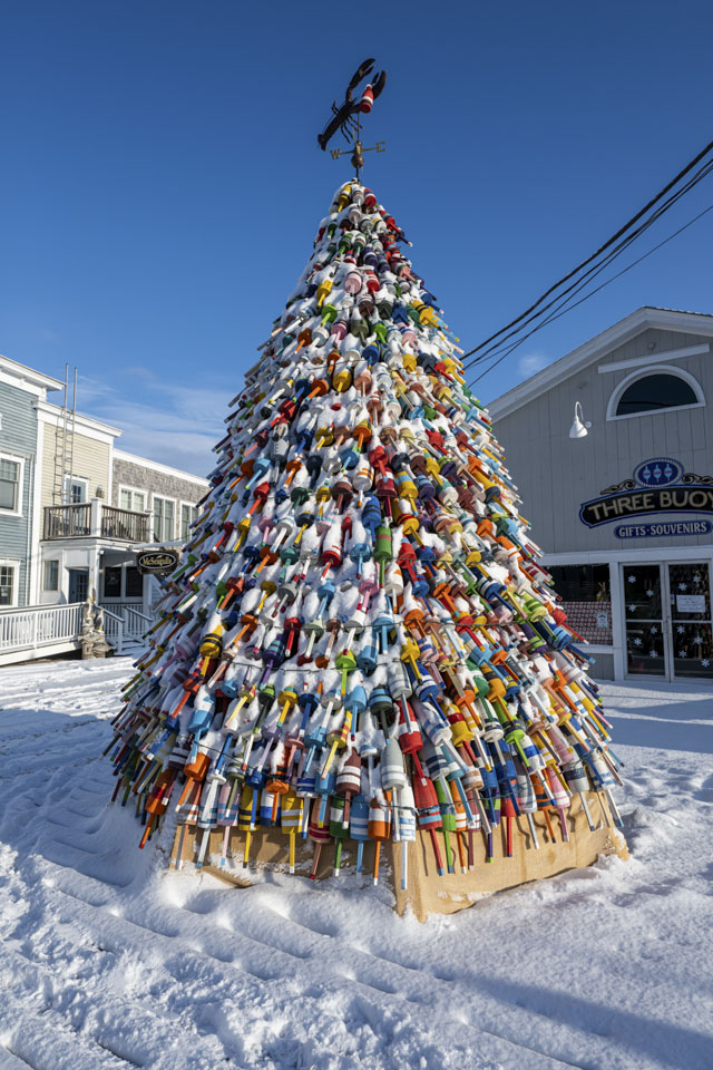 A tall cone-shaped outdoor decoration is covered with lobster buoys, and has a lobster weathervane at the top.