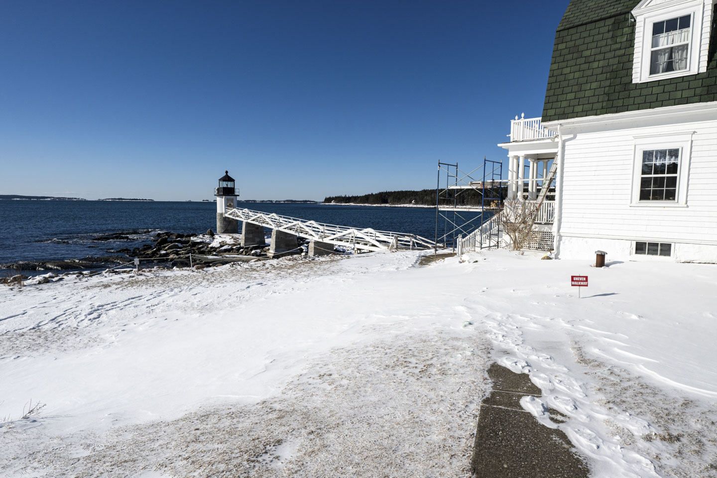 Marshall Point Lighthouse has snow on the ground, and metal scaffolding in front of the house.