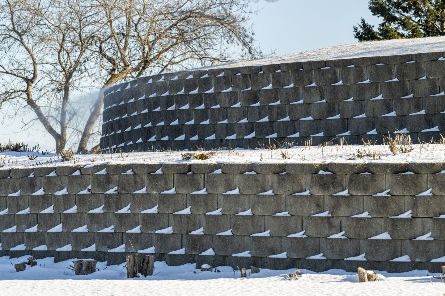 Some retaining walls have snow lodged on the cement bricks, and there is snow blowing off the top.
