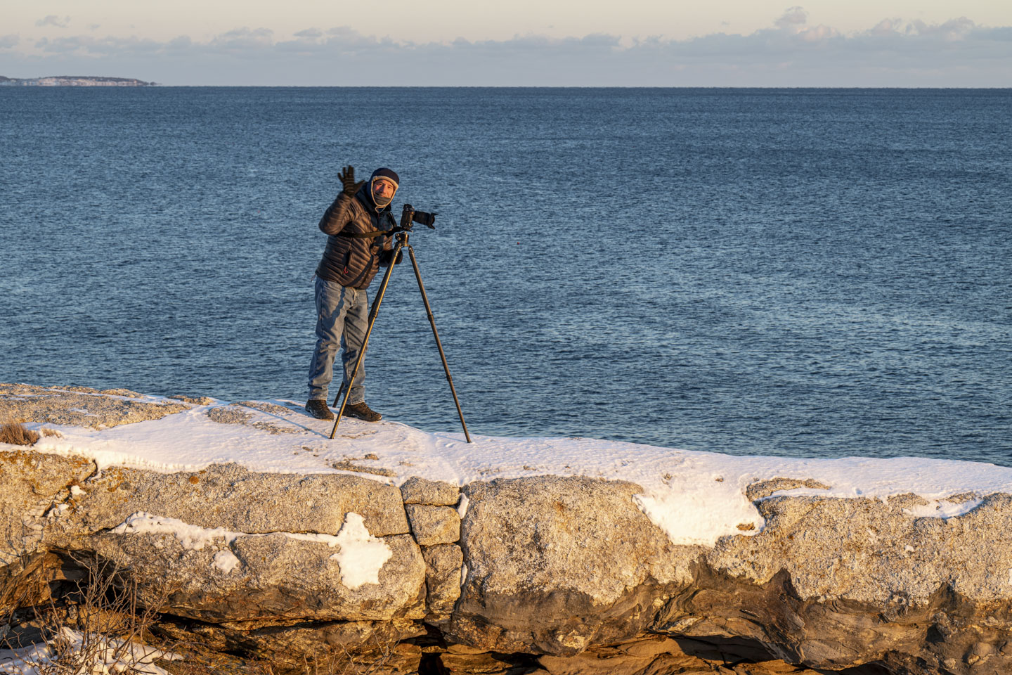 Paul is standing on some snow-covered rocks with his camera and tripod. He is bundled up against the cold.