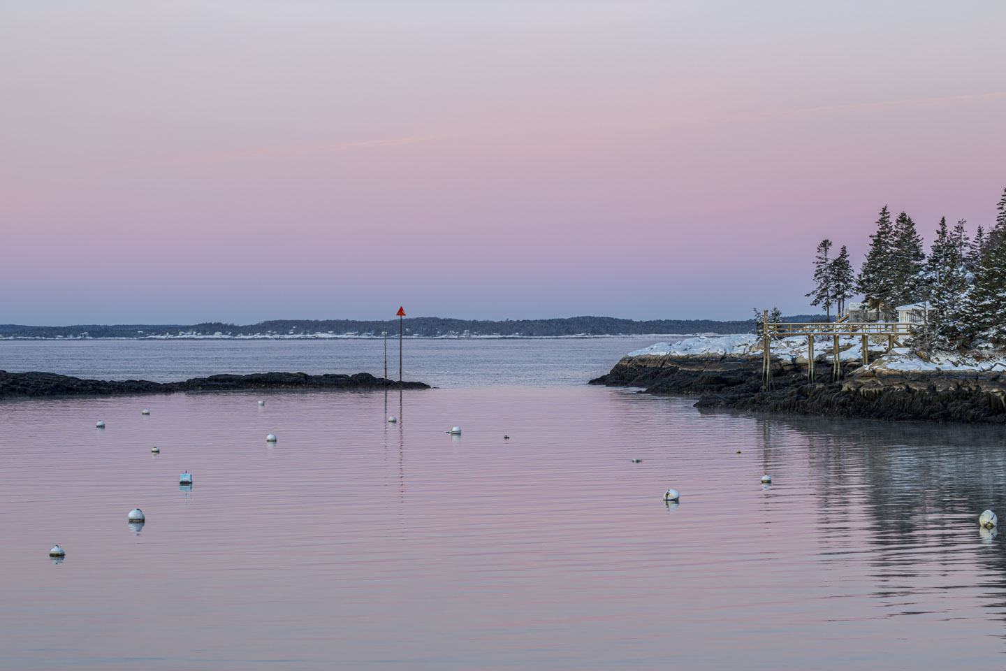 A pink glow is in the sky and is reflected on the water.
