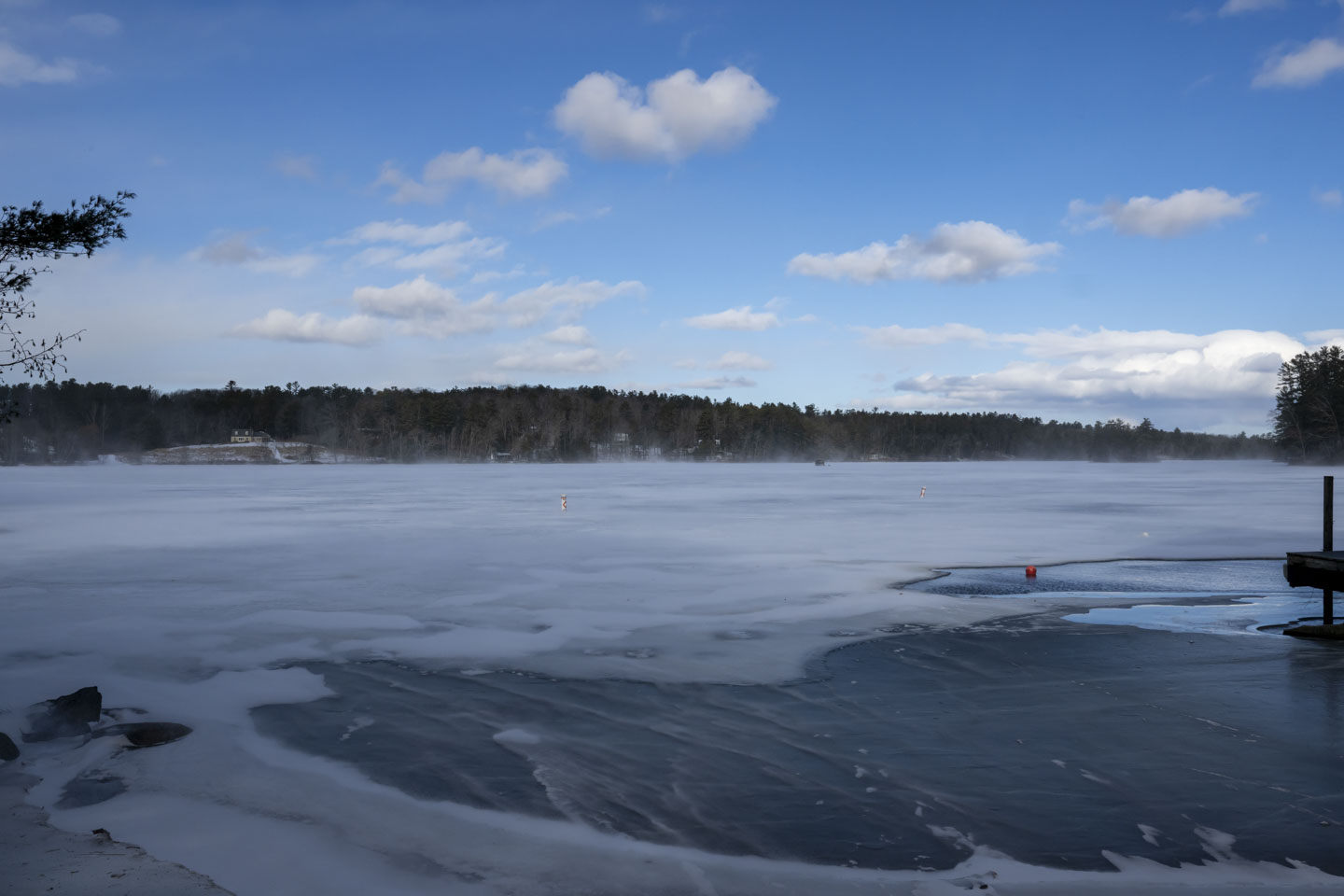 A blue sky with puffy clouds is above a wind-swept wide frozen river. 