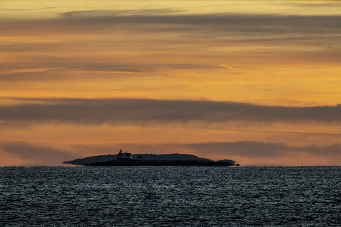 A view of Cuckolds Lighthouse with the light on, and a brilliant sky behind it.