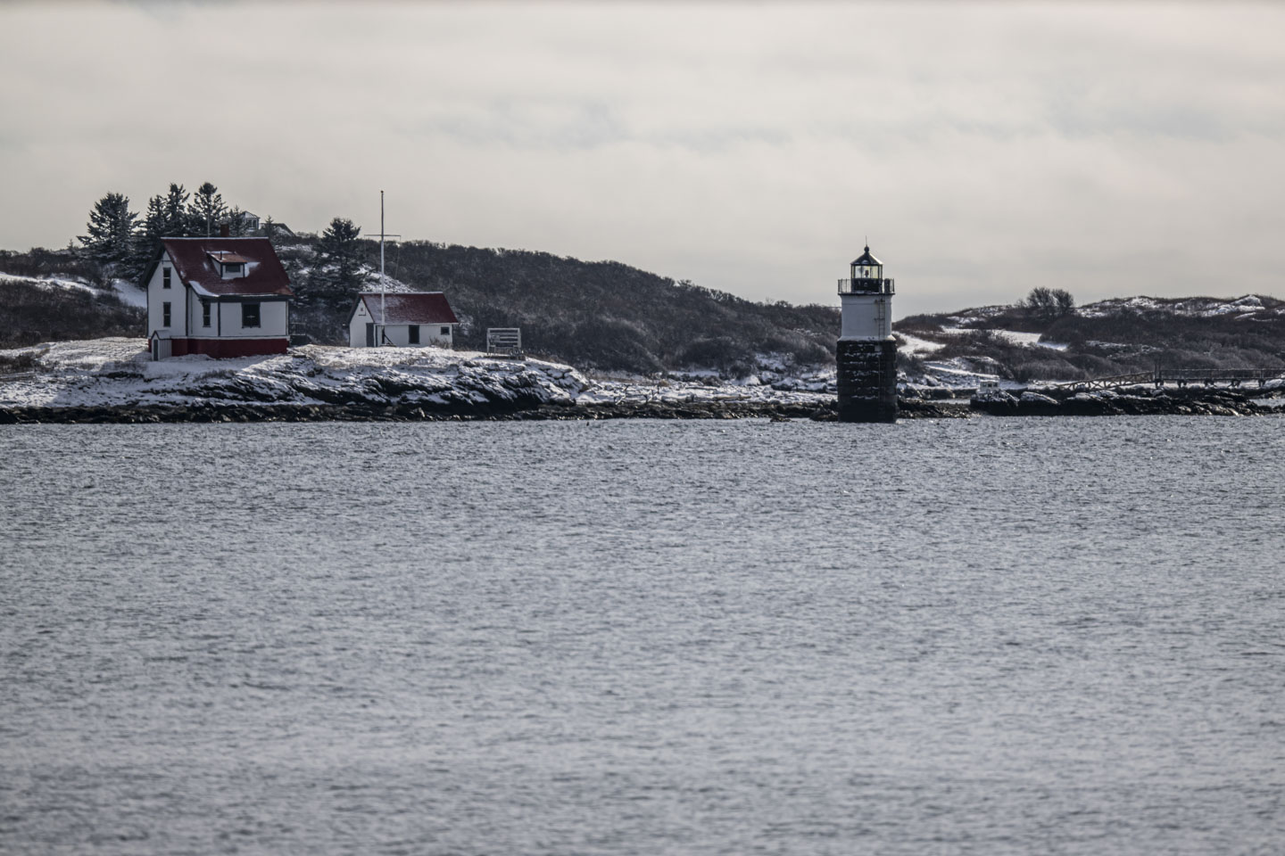 A lighthouse with a couple of small buildings is seen across a stretch of water.