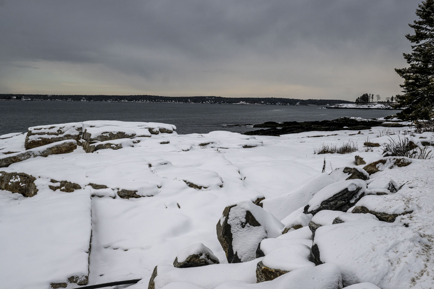 Snow covered rocks are in front of a relatively calm ocean.