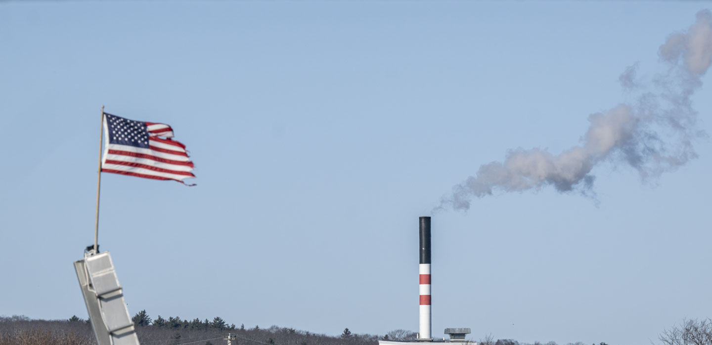 A flag is out straight in the wind, and steam from a smokestack is being blown away to the right.