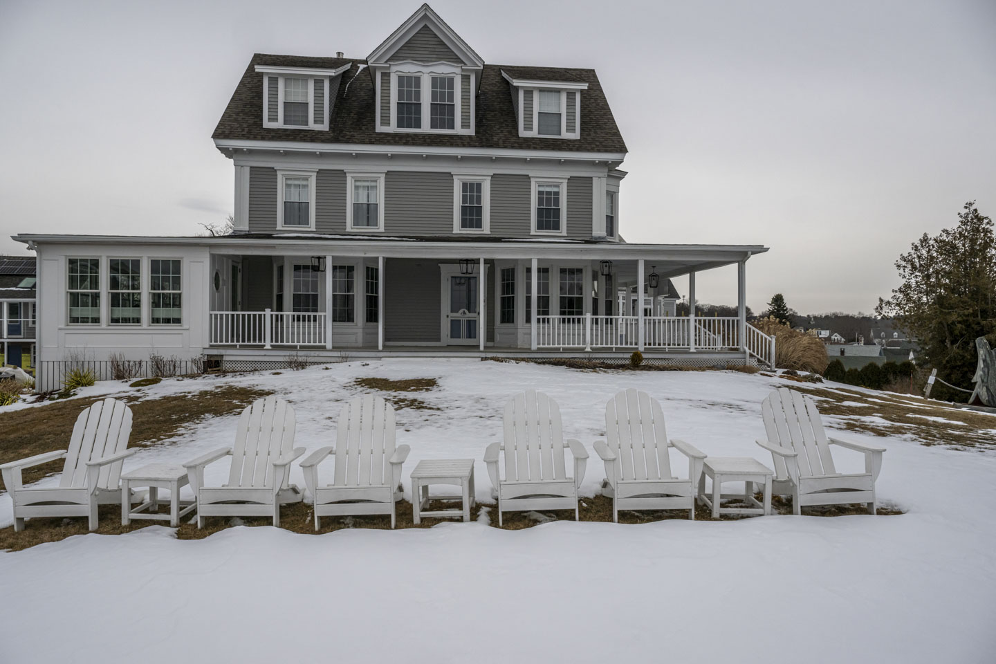 A view of Topside Inn from the lawn, with snow on the lawn. The Adirondak chairs are still set up.